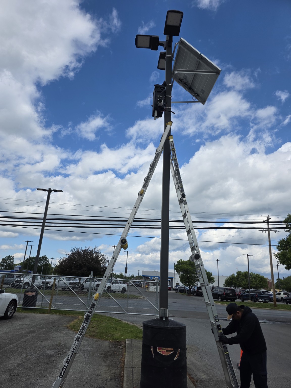Technician installing solar-powered surveillance equipment on a parking lot pole